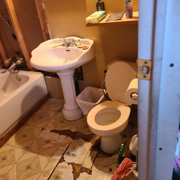 Bathroom before: damaged floor and pedestal sink