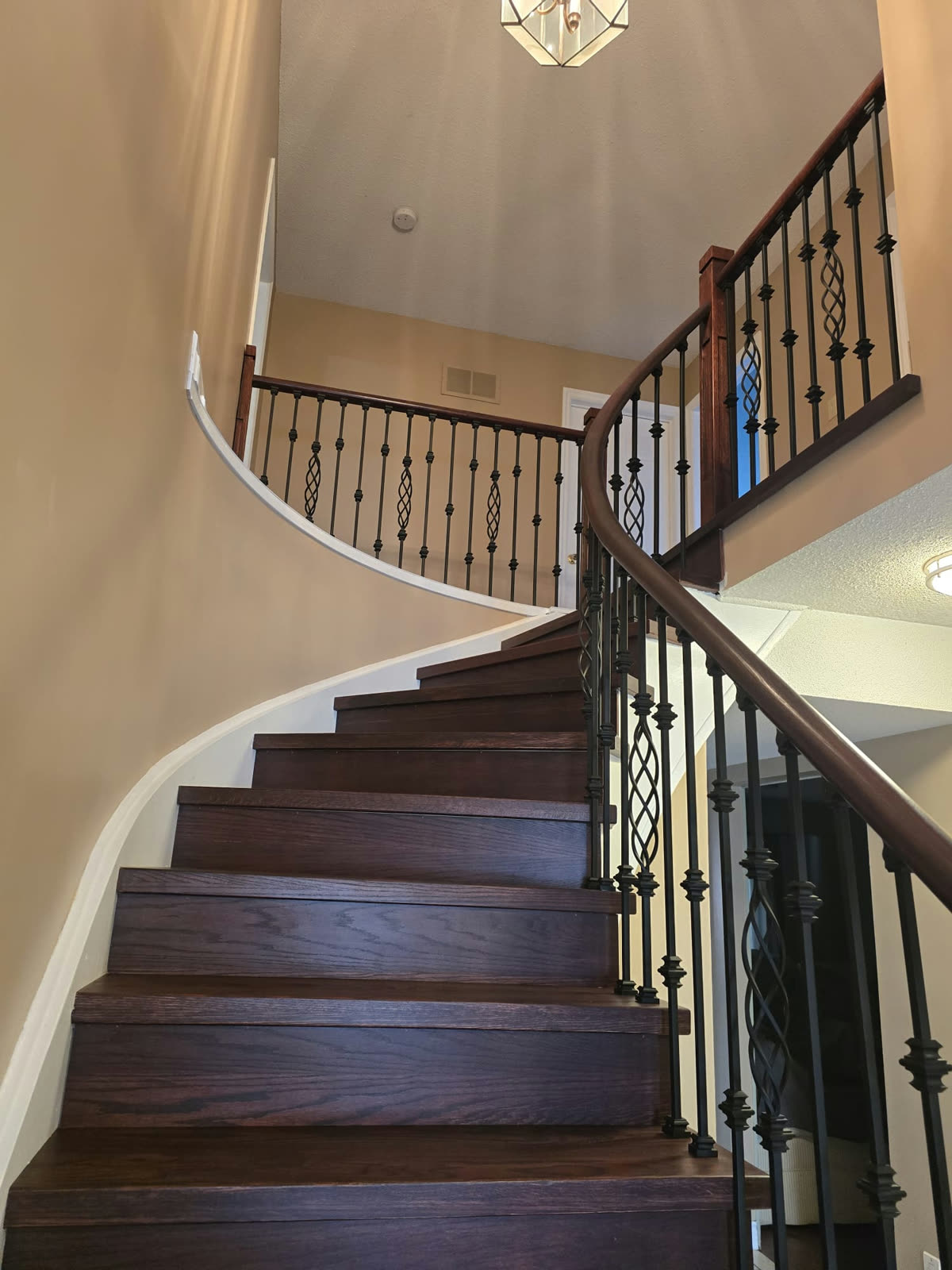 Finished curved staircase with dark hand rail and black iron balusters running up to the landing